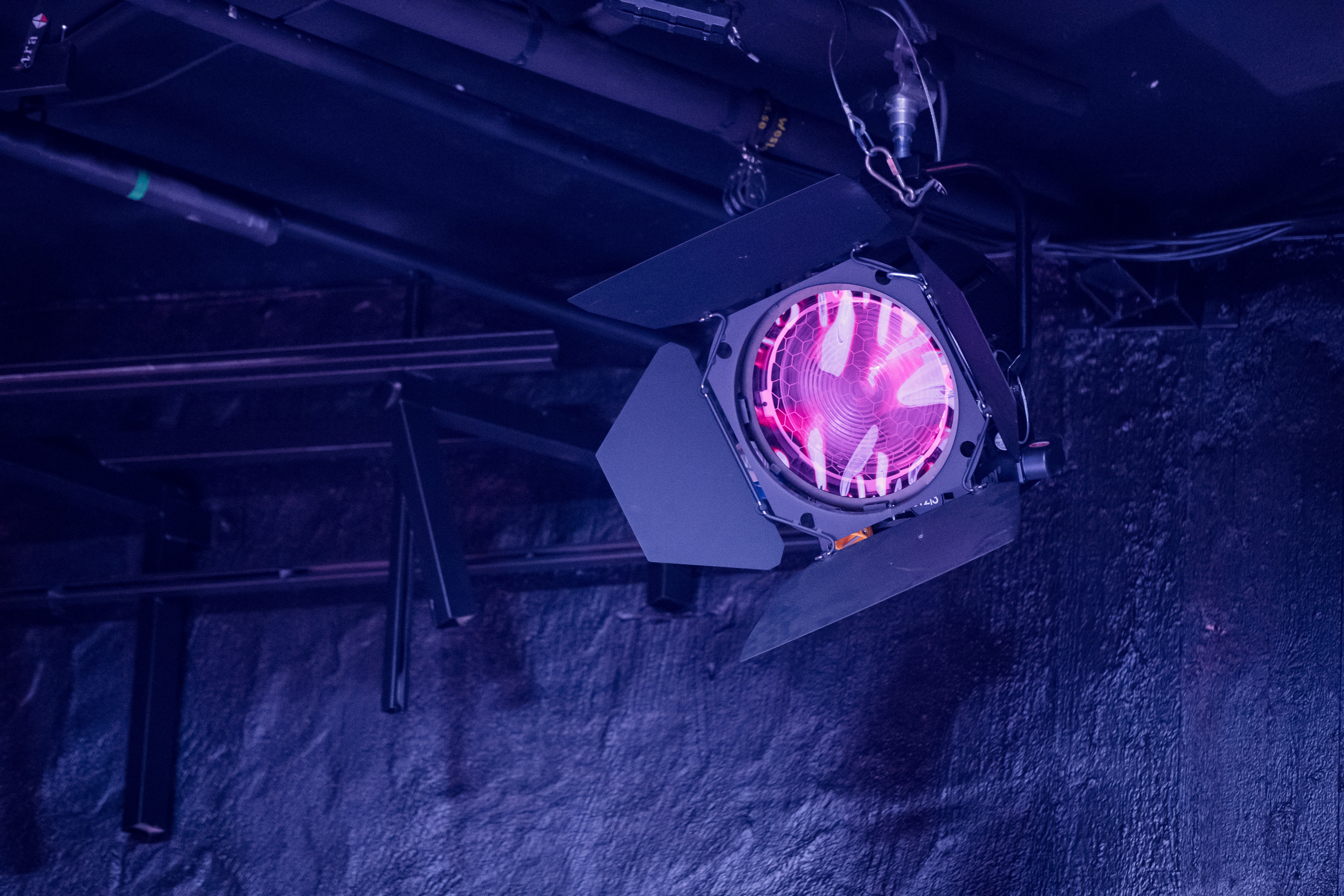 Strålkastare med rosa filmduk som reflekterar ett mörkt blå-lila ljus mot väggen.