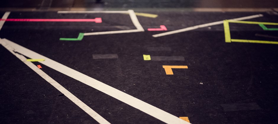 En mörk scen-matta som är tejpad med flera markeringar i färg. En mörk scen-matta som är tejpad med flera markeringar i färg.