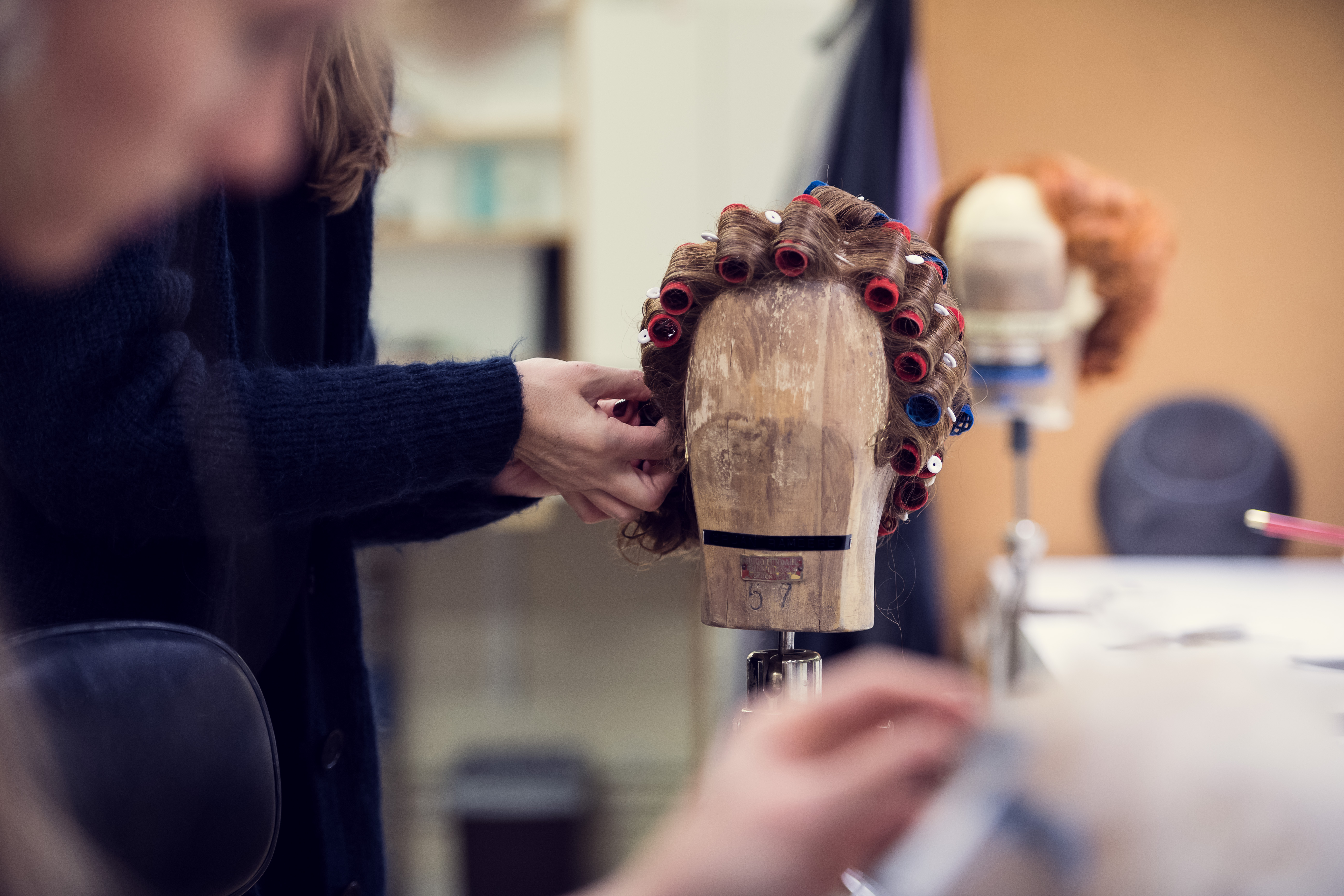 Perukmakare rullar håret på en provdocka.