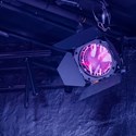Strålkastare med rosa filmduk som reflekterar ett mörkt blå-lila ljus mot väggen.