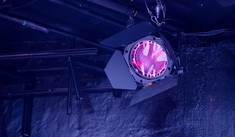 Strålkastare med rosa filmduk som reflekterar ett mörkt blå-lila ljus mot väggen.