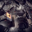 En liten lampa på ett notställ står i mitten på scenen omringat av orkesterns svarta tomma stolar.
